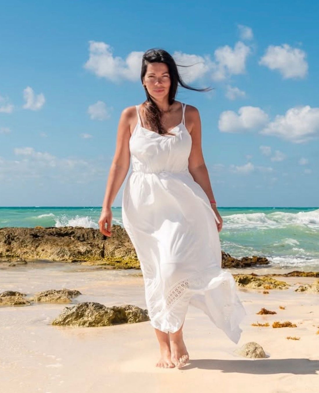 Yerthy Montes caminando por la playa con un vestido blanco